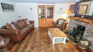 A living room with a herringbone wooden floor, a brown leather sofa, a white coffee table, a leather armchair, and a brick fireplace. - Greenhaven (Narberth)