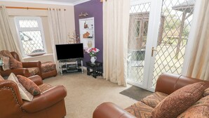 A living room with leather sofas, a flat-screen TV, and a small table with decorative items. - Greenhaven (Narberth)