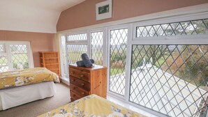 A bedroom with two beds, a wooden dresser, and large windows with metal grilles. - Greenhaven (Narberth)