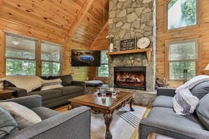 Un interior acogedor de cabaña con chimenea de piedra, paredes de madera y un televisor.