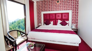 Une chambre d’hôtel avec un grand lit, une chaise, une petite table avec un vase, et une vue sur les montagnes par la fenêtre.