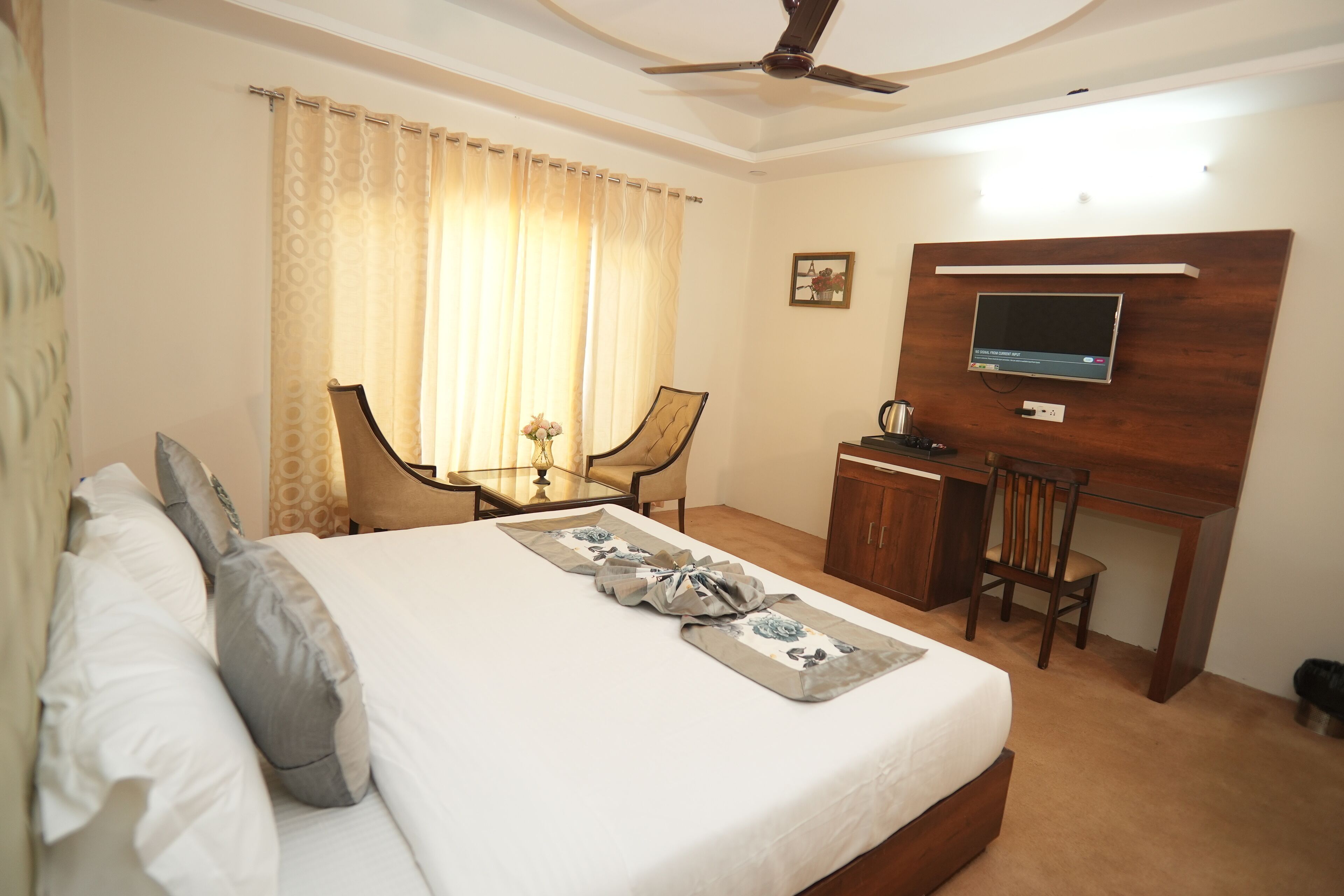 A hotel room with a bed, a desk, a chair, a television, and a ceiling fan.
