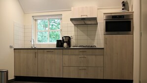 Een moderne keuken met houten kastjes, een inbouwoven en een raam dat voor natuurlijk licht zorgt.