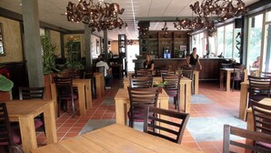 Een restaurant met houten tafels en stoelen, een bar en grote ramen die natuurlijk licht binnenlaten.