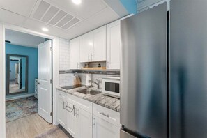 Una cocina moderna con armarios blancos, un refrigerador de acero inoxidable, un microondas y un lavamanos.
