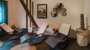 Ein Spa-Raum mit vier Liegen, einem großen Spiegel, einem Gemälde und einer Steinskulptur.