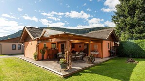 Ein Holzhaus mit überdachter Terrasse, Feuerstelle und gepflegtem Rasen.
