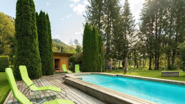 Eine Holzterrasse mit Swimmingpool, umgeben von hohen Bäumen und einer Holzhütte.