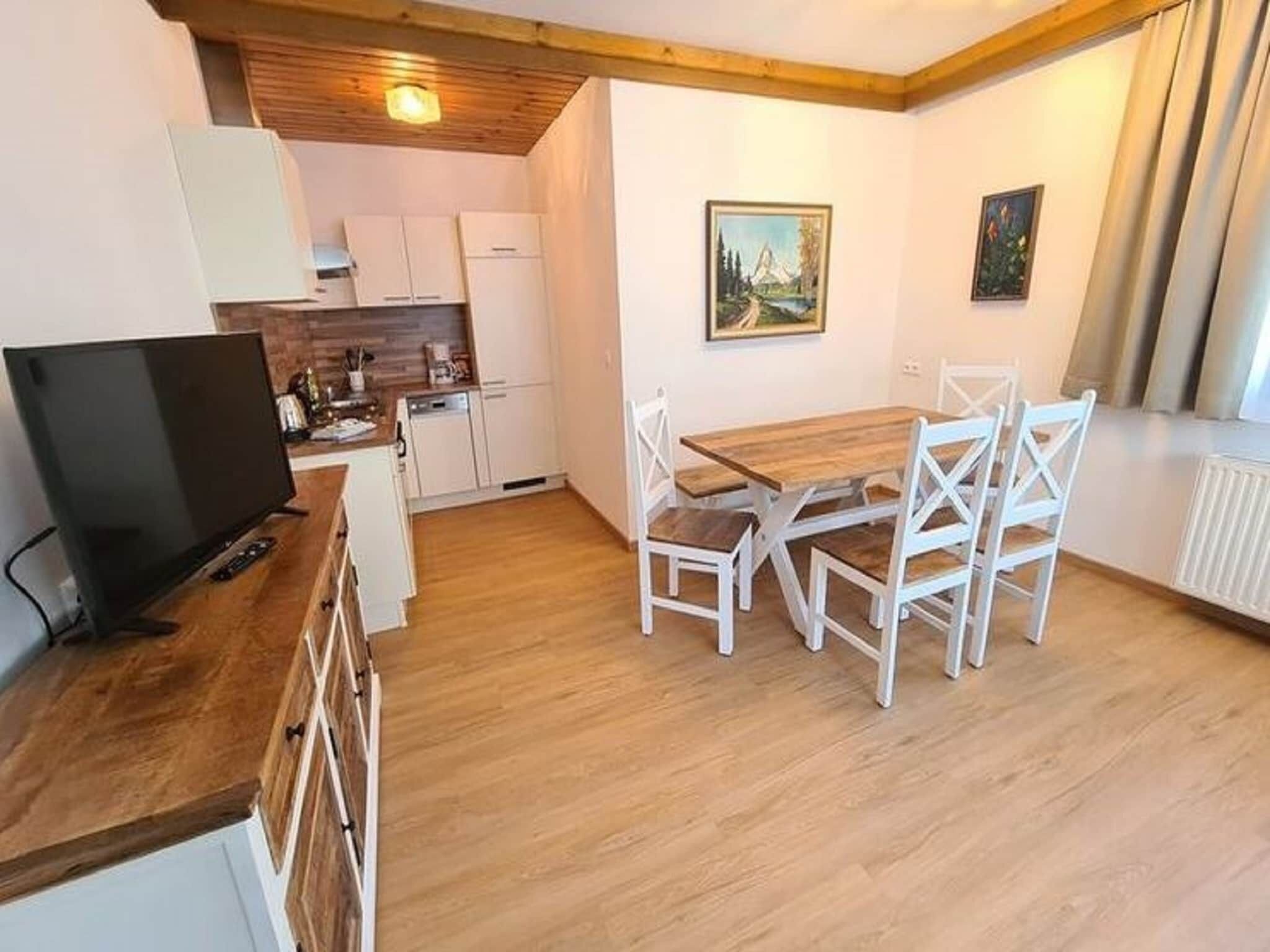 A compact kitchen with white cabinets, a wooden dining table with white chairs, and a painting on the wall.