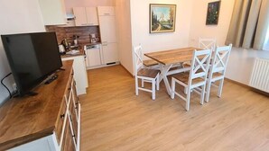 A compact kitchen with white cabinets, a wooden dining table with white chairs, and a painting on the wall. - Cosy apartment in Bad Kleinkirchheim (Bad Kleinkirchheim)