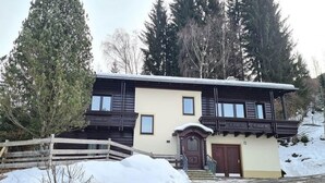 A two-story building with a wooden facade, a balcony, and a snow-covered ground. - Cosy apartment in Bad Kleinkirchheim (Bad Kleinkirchheim)