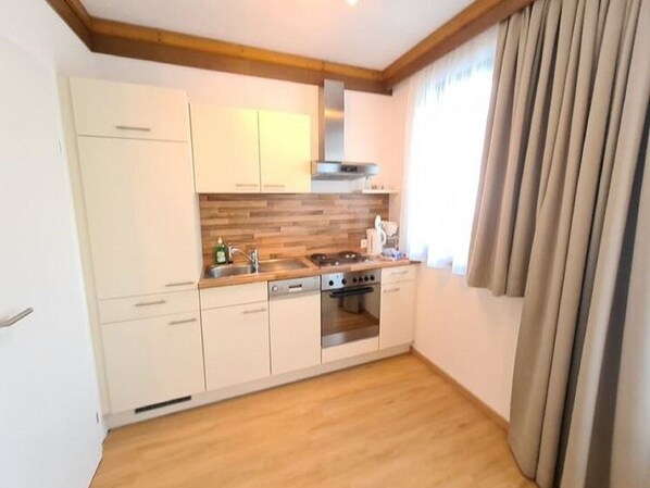 Cocina compacta con gabinetes blancos, encimera de madera, estufa y ventana con cortinas.