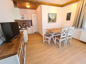 A compact kitchen with white cabinets, a wooden dining table with white chairs, and a painting on the wall.