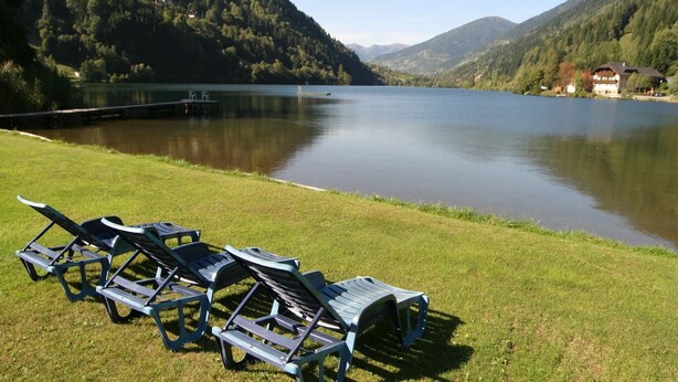 A lakeside view with lounge chairs on a grassy area. - Nice apartment in Bad Kleinkirchheim (Bad Kleinkirchheim)