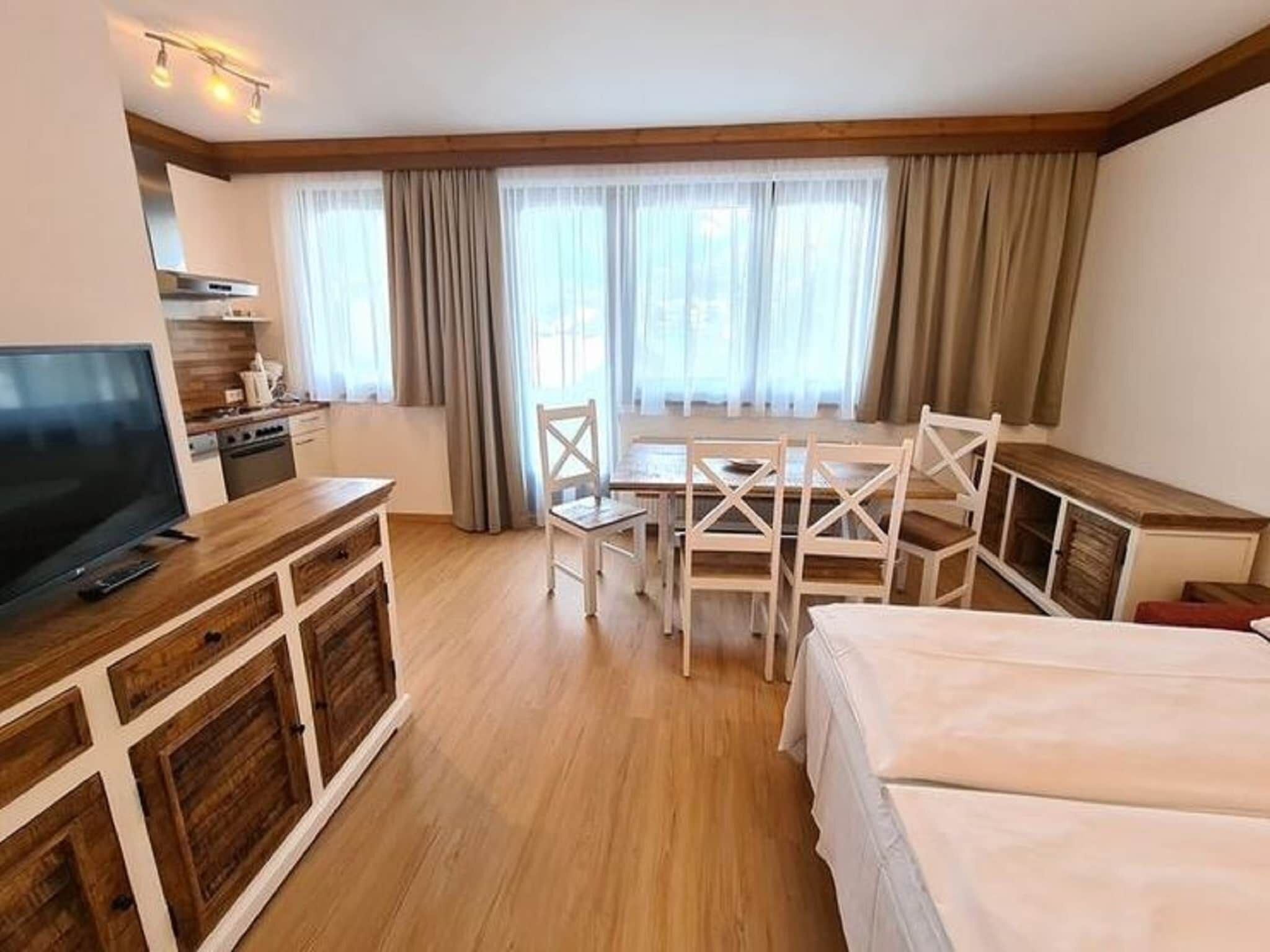Een hotelkamer met een houten vloer, een televisie op een houten kast, een eettafel met stoelen, en een bed.