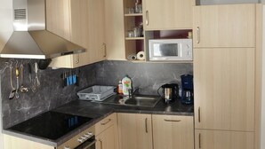 Una cocina compacta con armarios de madera, encimera negra, campana extractora de acero inoxidable, microondas, cafetera y lavavajillas.