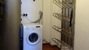 Un lavadero pequeño con lavadora y secadora de carga frontal, un tendedero metálico y un calentador de agua de gran tamaño.