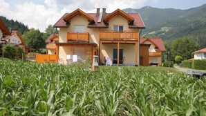 A two-story house with a balcony, surrounded by a cornfield, set against a mountainous backdrop. - Chalet in Koetschach-Mauthen near ski slope (Kötschach-Mauthen)