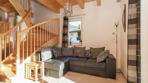 A modern living room with a wooden staircase, a sectional sofa with patterned cushions, and a view of the outdoors through a window. - Chalet in Koetschach-Mauthen near ski slope (Kötschach-Mauthen)