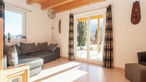 A spacious living room with a wooden ceiling, a sofa with patterned cushions, a wooden side table, and a view through large glass doors to the outdoors. - Chalet in Koetschach-Mauthen near ski slope (Kötschach-Mauthen)