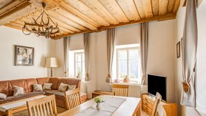A cozy living room with a wooden ceiling, a sofa set, a dining table, and a television.