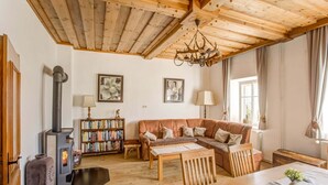 A cozy living room with a wooden ceiling, a fireplace, a sofa, a table, and a bookshelf.