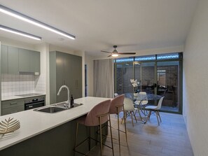 A modern kitchen with a central island, bar stools, and a dining area with a glass table and chairs. - Supremely Spacious @Kingston (Kingston)
