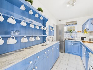 Een keuken met blauwe kastjes, witte aanrechtbladen en witte bekers die hangen.