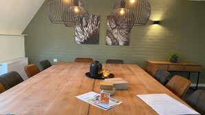 Een vergaderzaal met een lange houten tafel, lederen stoelen en hanglampen.