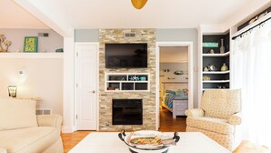 A living room with a fireplace, a dining table with a roast, a sofa, and a patterned armchair.