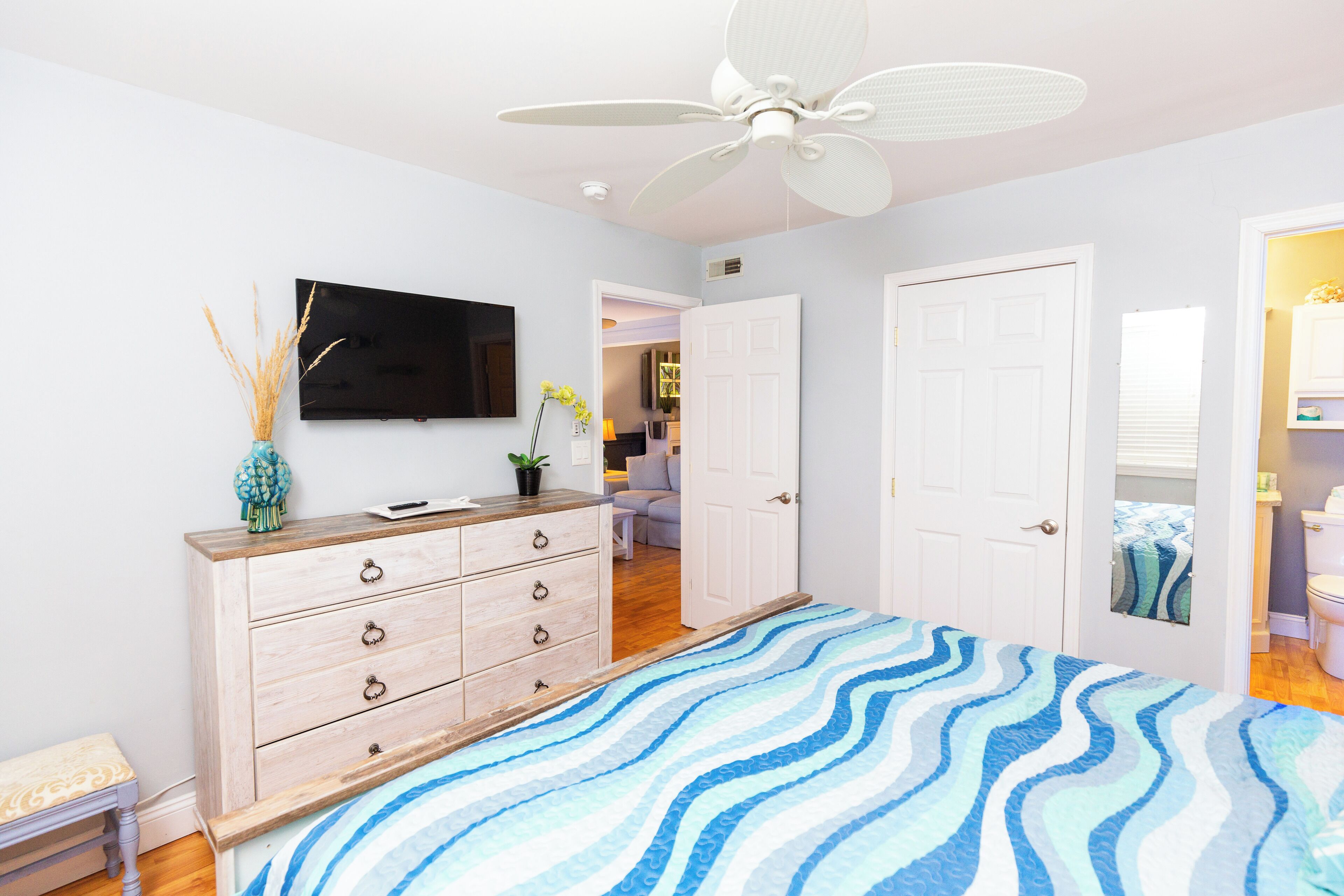 Une chambre à coucher avec un lit, une commode, un téléviseur et un ventilateur de plafond.