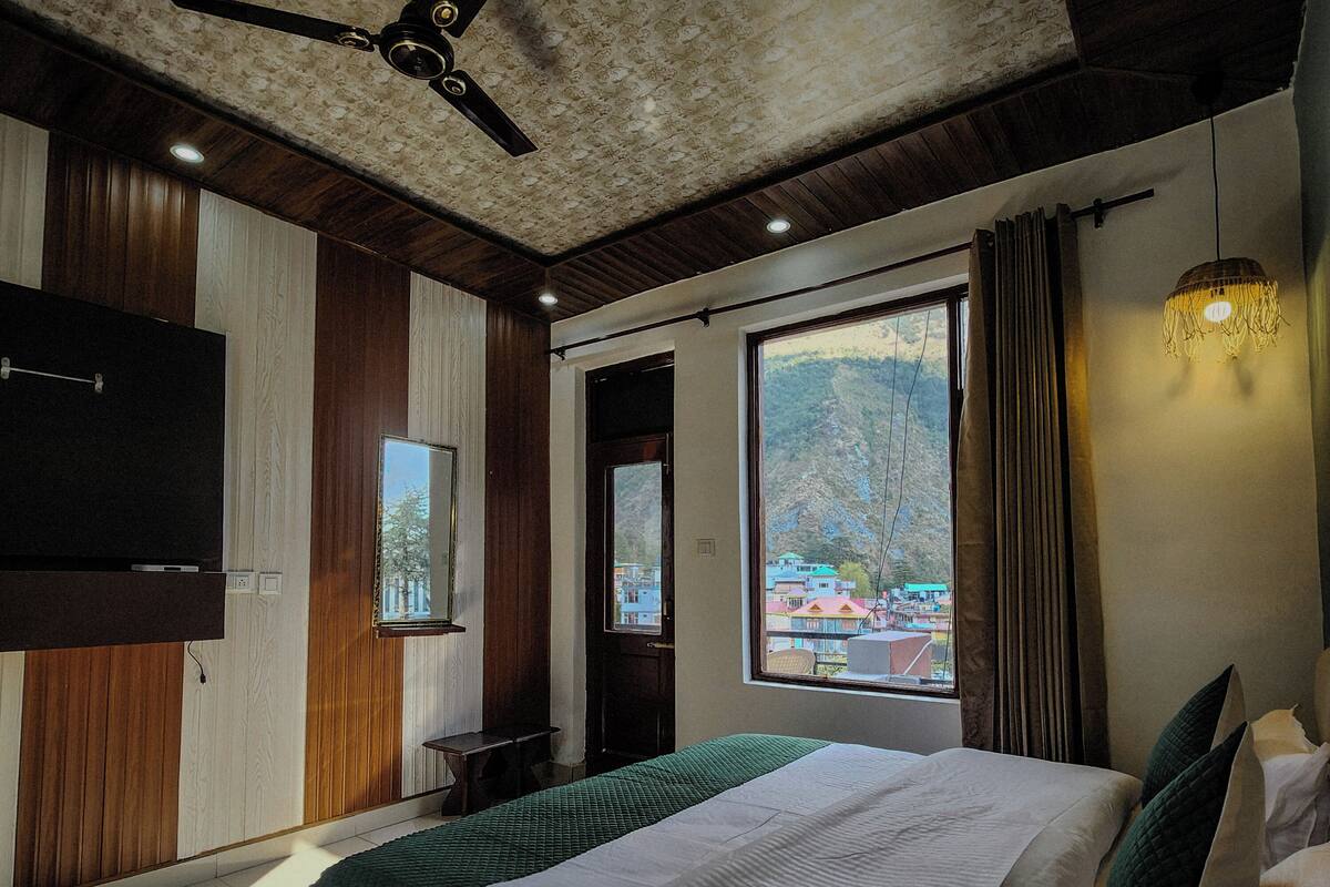 A hotel room with a bed, a ceiling fan, a large window with a view, and a TV on the wall.