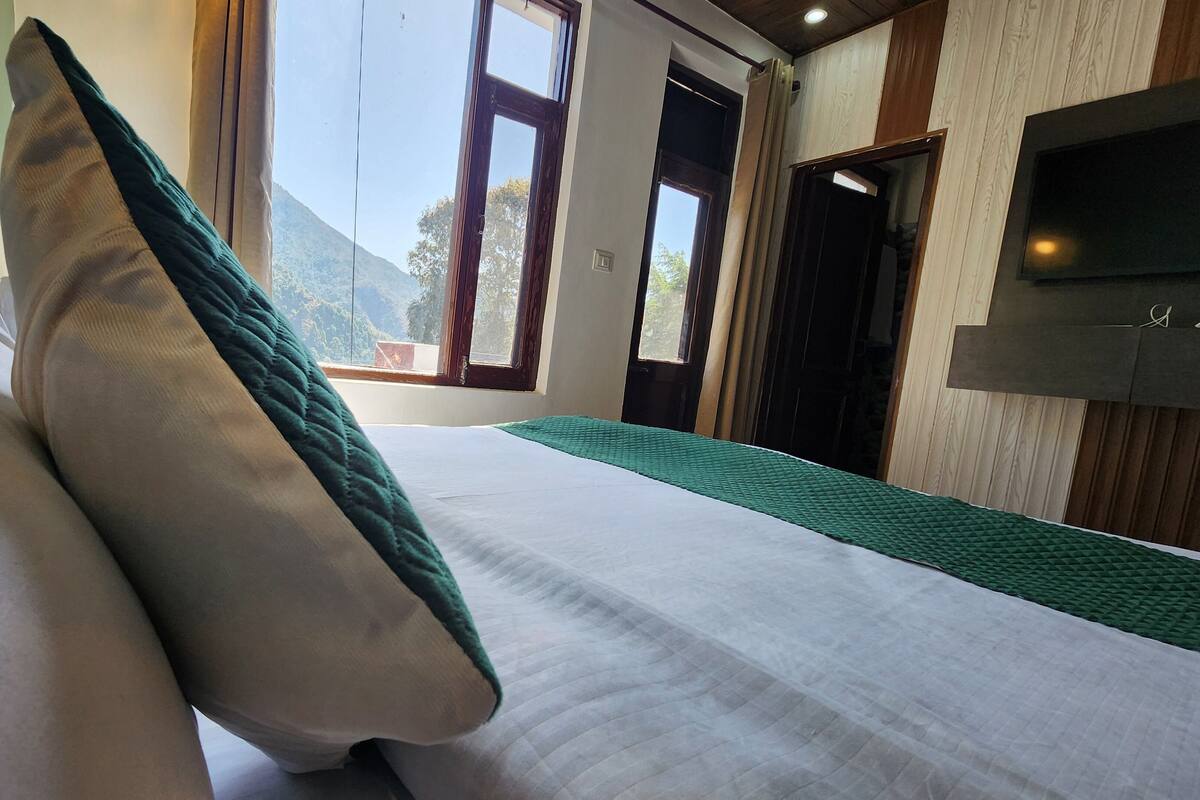 A neatly made bed with a green and white pillow, a green throw blanket, and a view of a mountainous landscape through a window.