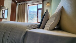 A bed with a view of mountains through a window, a hanging light fixture, and wooden paneling on the walls. - Hotel Mahadev (Dharamshala)