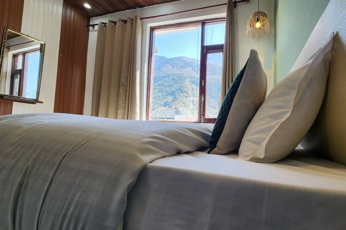 A bed with a view of mountains through a window, a hanging light fixture, and wooden paneling on the walls.