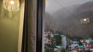 A view from a window overlooking a town with buildings and mountains in the background. - Hotel Mahadev (Dharamshala)