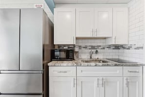 A kitchen with white cabinets, a stainless steel refrigerator, a microwave, and a tiled backsplash.