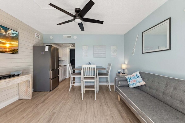 A compact living space with a kitchenette, dining area, and a sofa with a cushion.