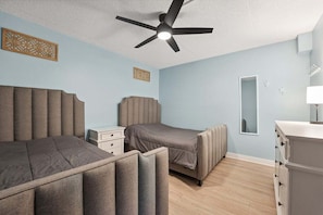 A bedroom with a bed, bedside table, dresser, ceiling fan, and decorative wall panels.