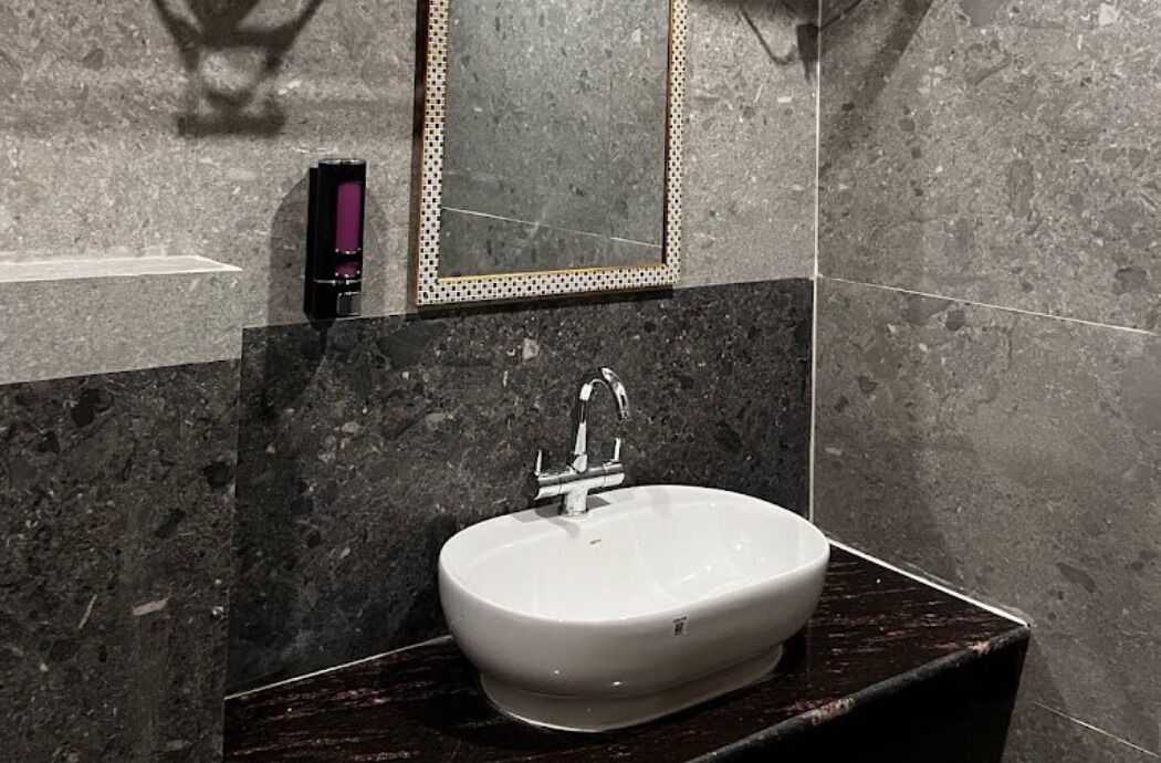 A bathroom with a white sink, dark marble countertop, and a mirror with a decorative frame.