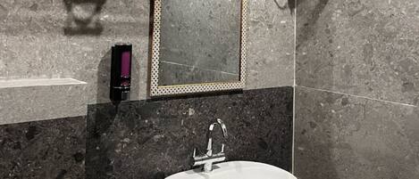 A bathroom with a white sink, dark marble countertop, and a mirror with a decorative frame.