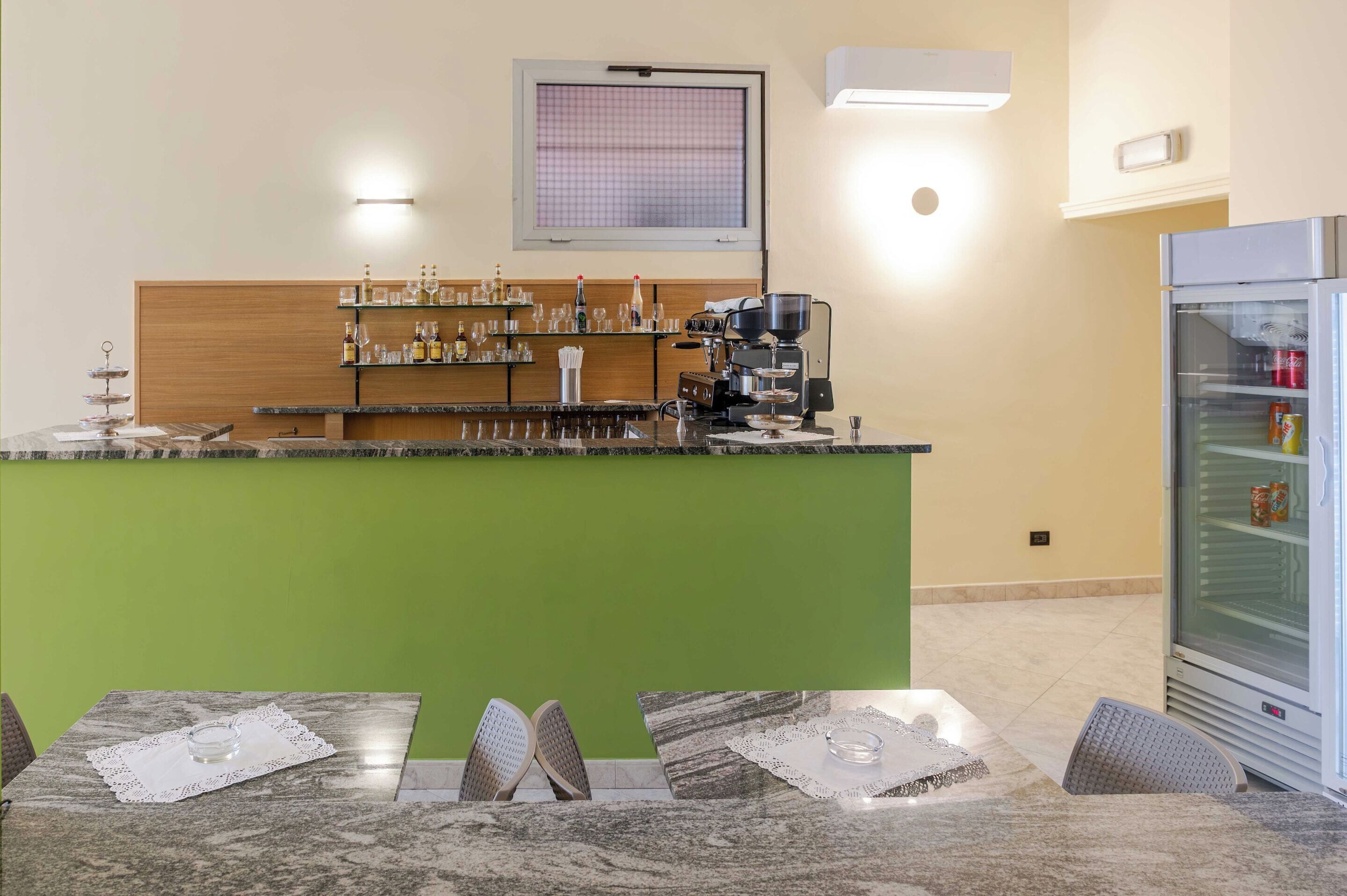 Eine Bar mit einem grünen Tresen, einer Kaffeemaschine und Regalen mit Flaschen und Gläsern.