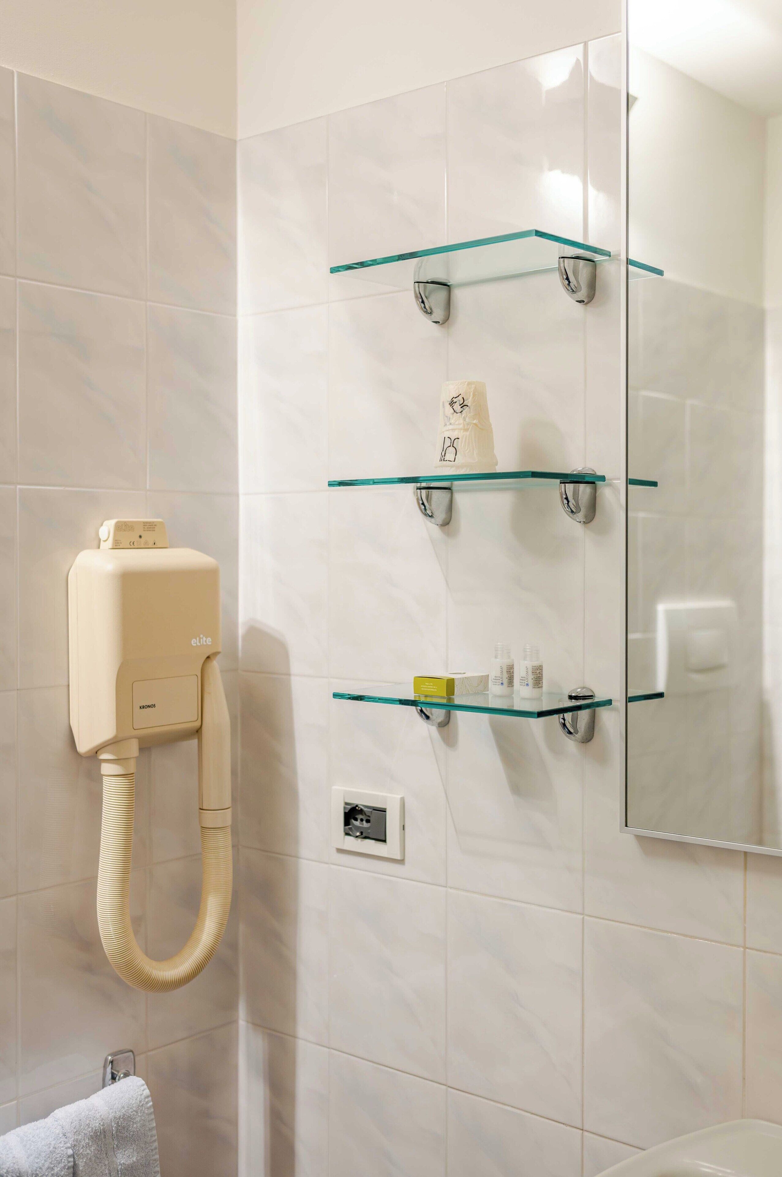Un baño con secador de pelo, estantes de vidrio y un espejo.