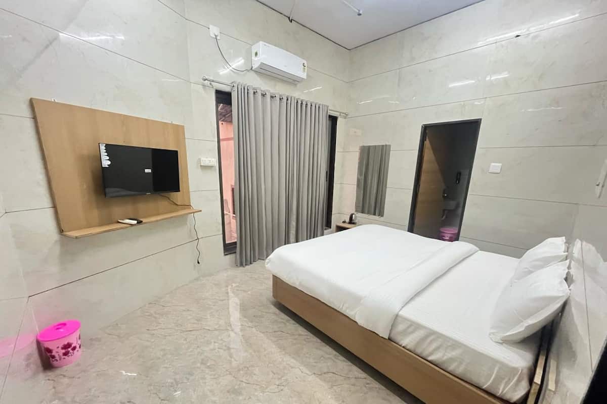 A modern hotel room with a large bed, a mounted TV, a small bedside table, and a mirror.