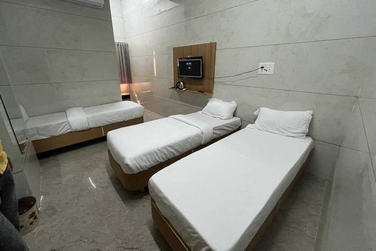 A hotel room with two single beds, a TV mounted on the wall, and a small shelf with a kettle.
