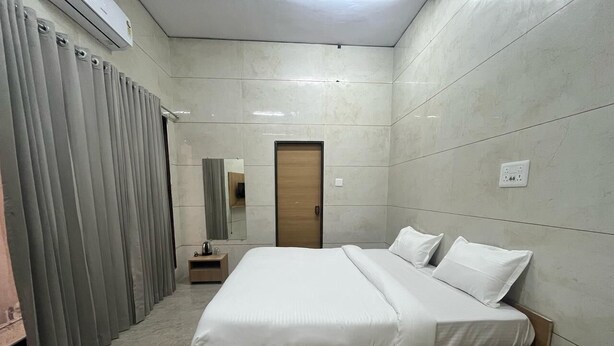 Een moderne hotelkamer met een groot bed, een houten hoofdbord, een klein nachtkastje en een garderobe met grijze gordijnen.