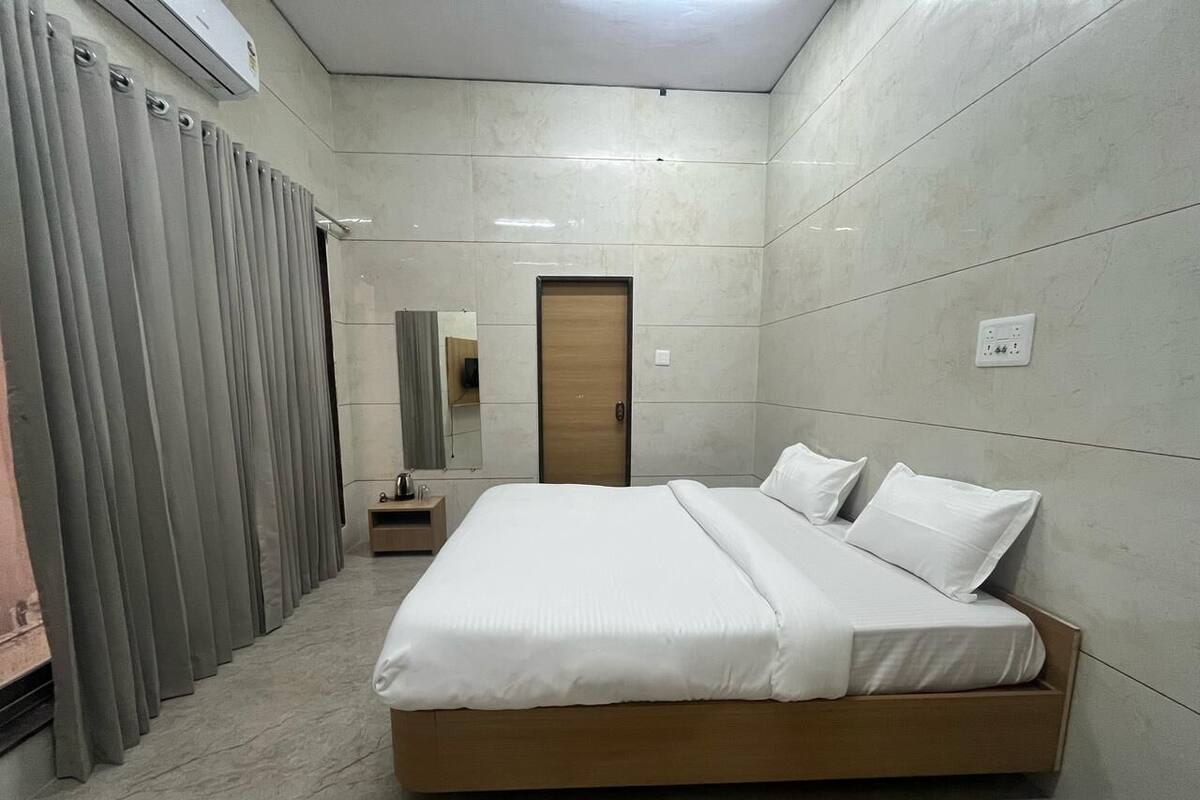A modern hotel room with a large bed, a wooden headboard, a small bedside table, and a wardrobe with grey curtains.