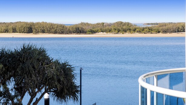 A coastal view with a clear sky, a sandy beach, and dense vegetation in the background.