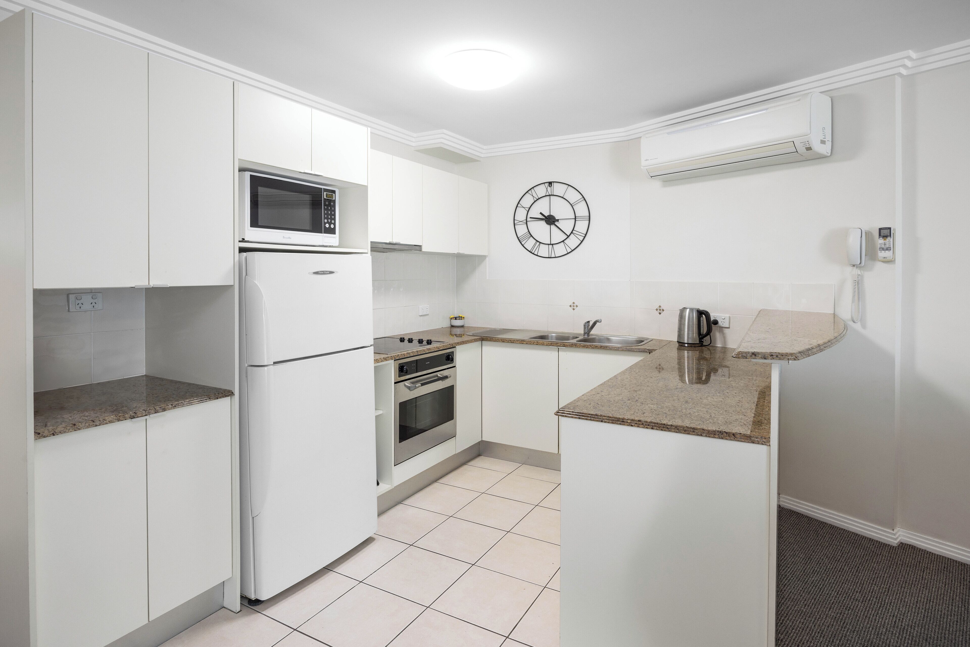 Eine moderne Küche mit weißen Schränken, einer Mikrowelle, einem Backofen und einer Wanduhr.