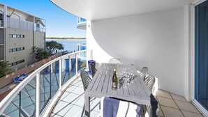 A balcony with a table set for dining, overlooking a body of water and a building.